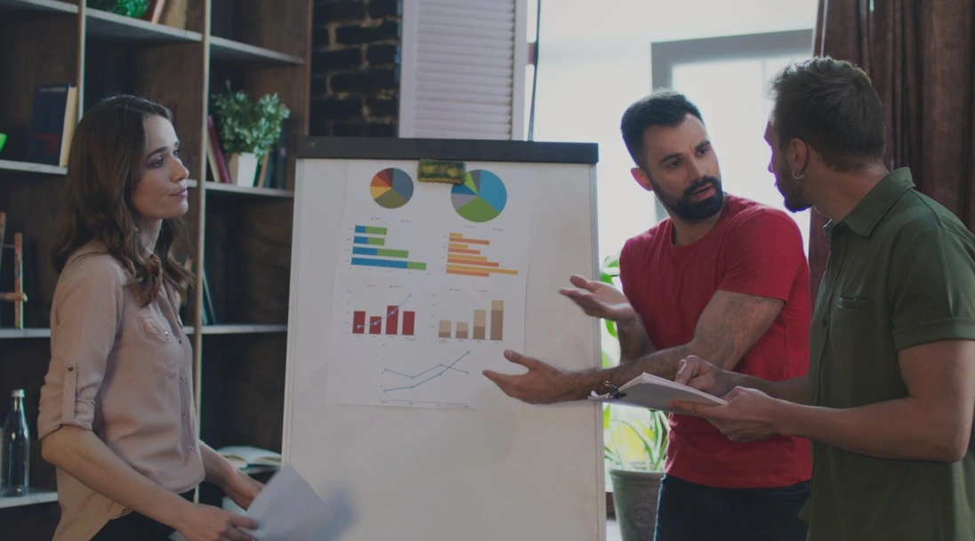 Group discussion in office with charts and graphs displayed on flipchart, team members debating insights from the data.