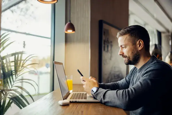 Man working on laptop at café table with notebook and coffee